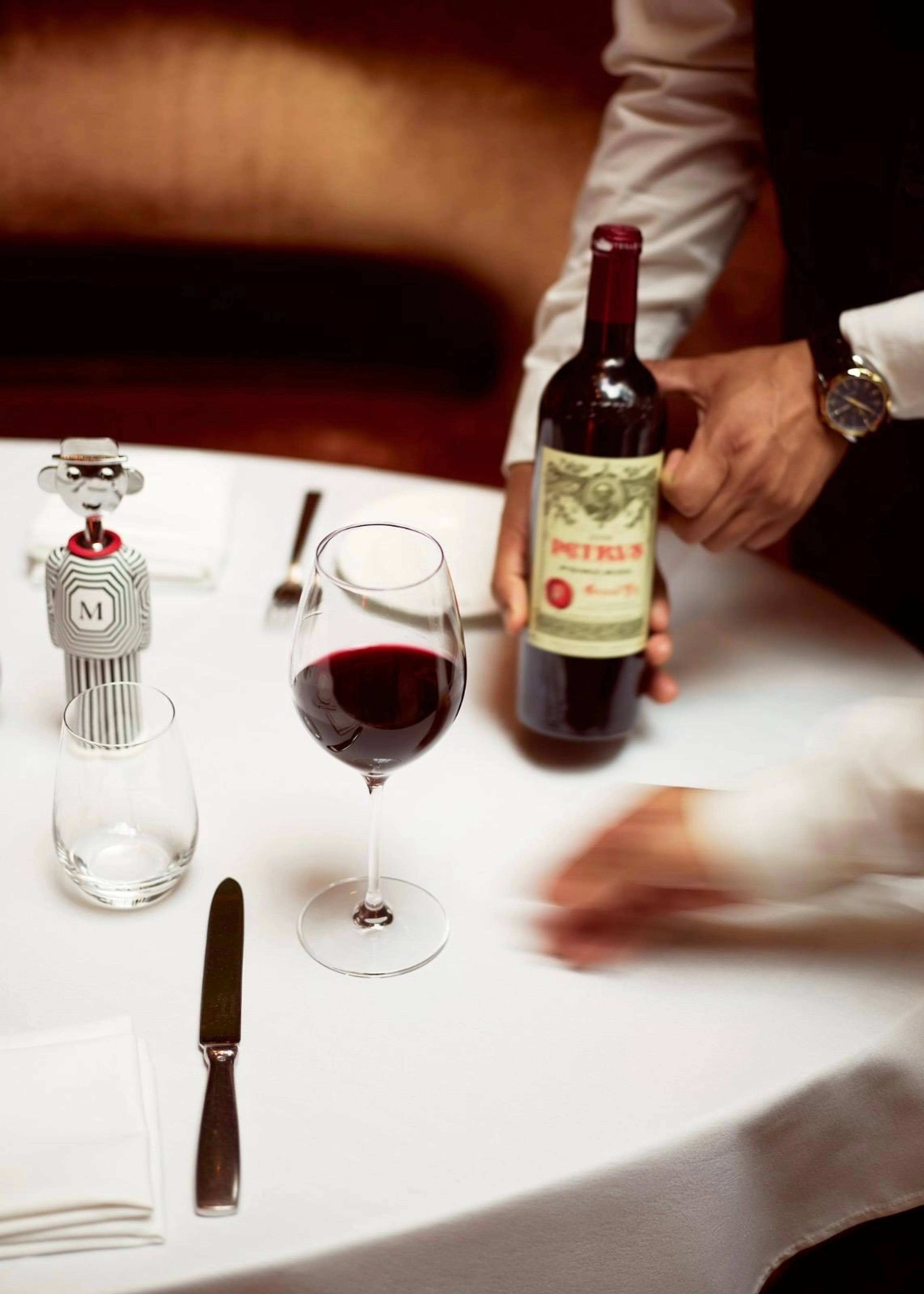 Ein elegant gedeckter Tisch im Hotel The Mark mit einem Glas Rotwein, einer Flasche Petrus Wein und dem schwarz-weiß gestreiften Alessi Alessandro M. Korkenzieher mit einem M auf der Brust.