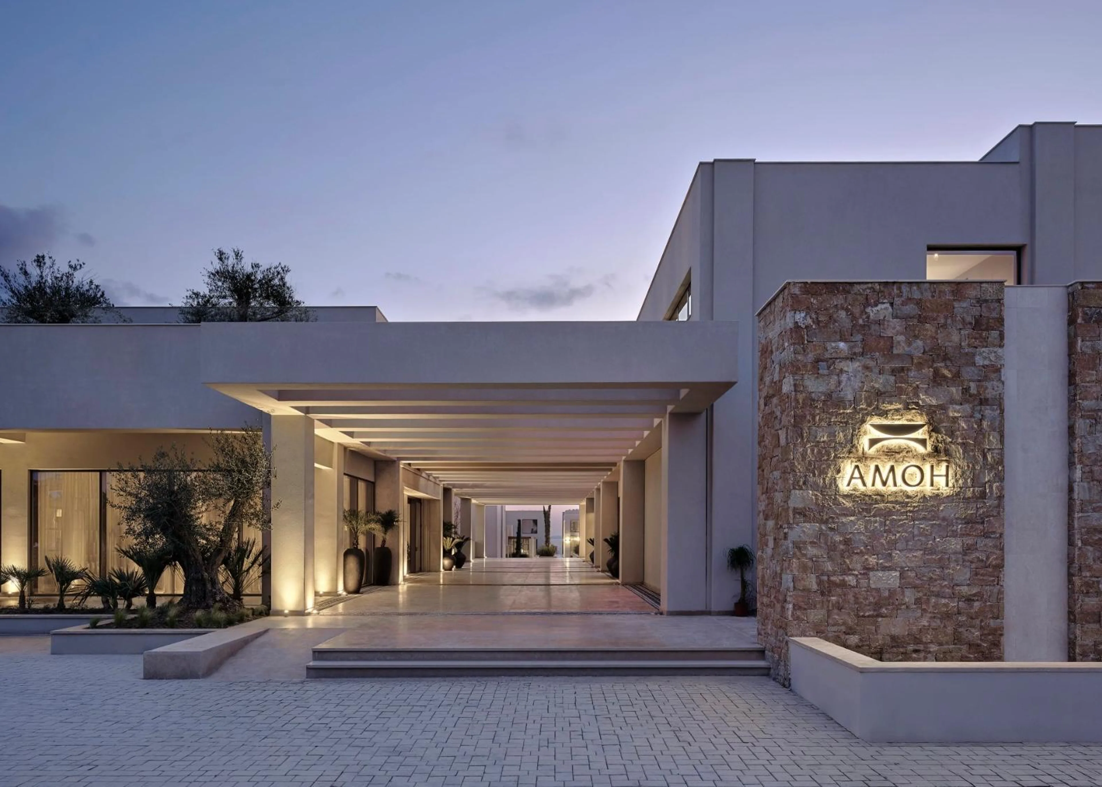 Außenansicht des AMOH Luxury Collection Resort auf Rhodos in der Dämmerung mit moderner Architektur, Natursteinfassaden und stimmungsvoller Beleuchtung.
