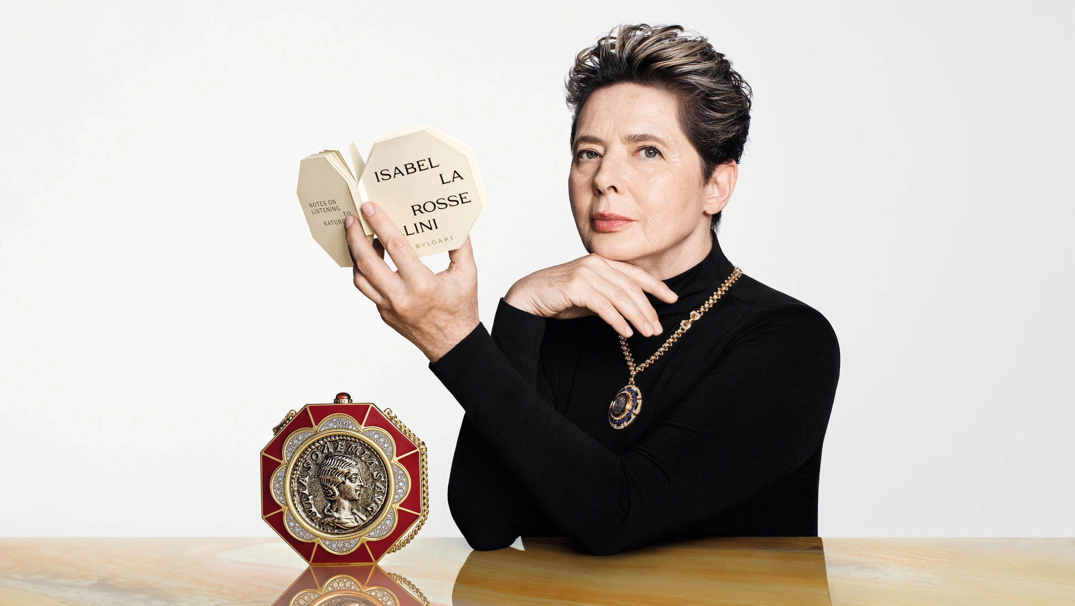 Isabella Rossellini mit Miniaturbuch und Bulgari Monete Minaudière aus der Icons Minaudière Kollektion
