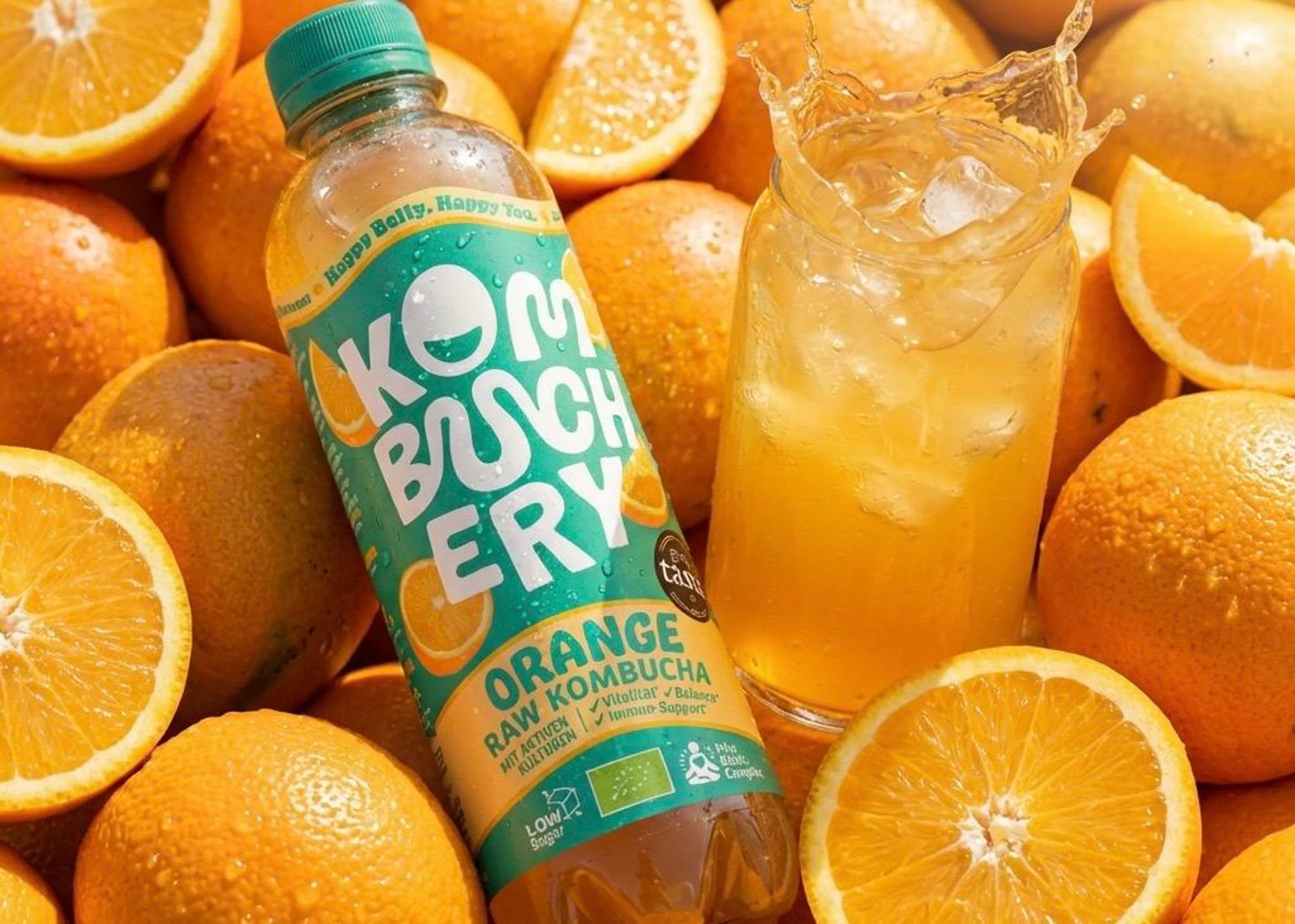 Flasche Bio-Kombucha Orange von Kombuchery auf frischen Orangen arrangiert.