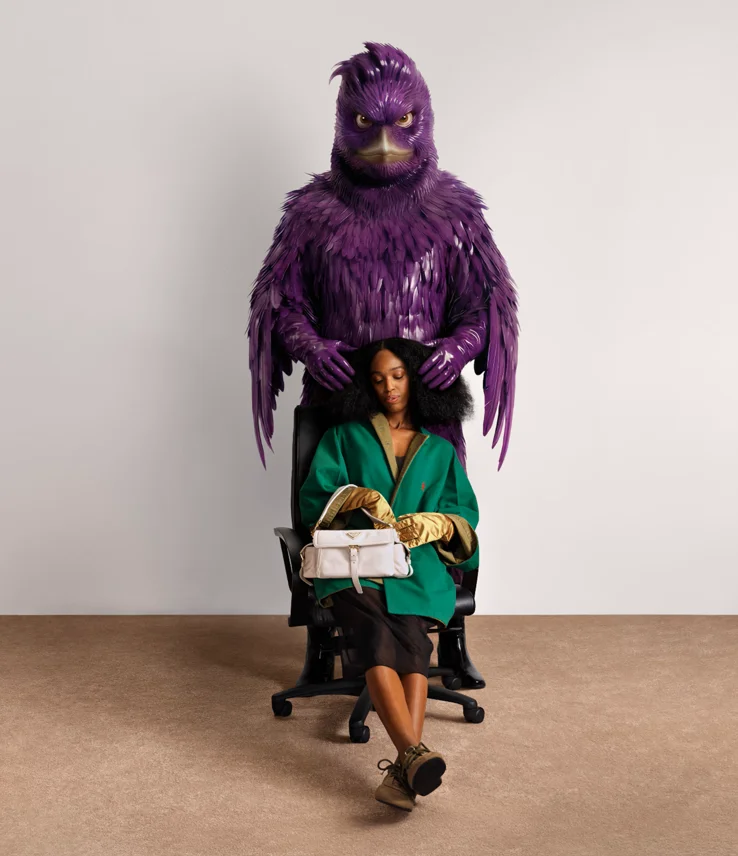 Weibliches Model mit weißer Prada Tasche sitzt vor großer lila Vogel-Figur