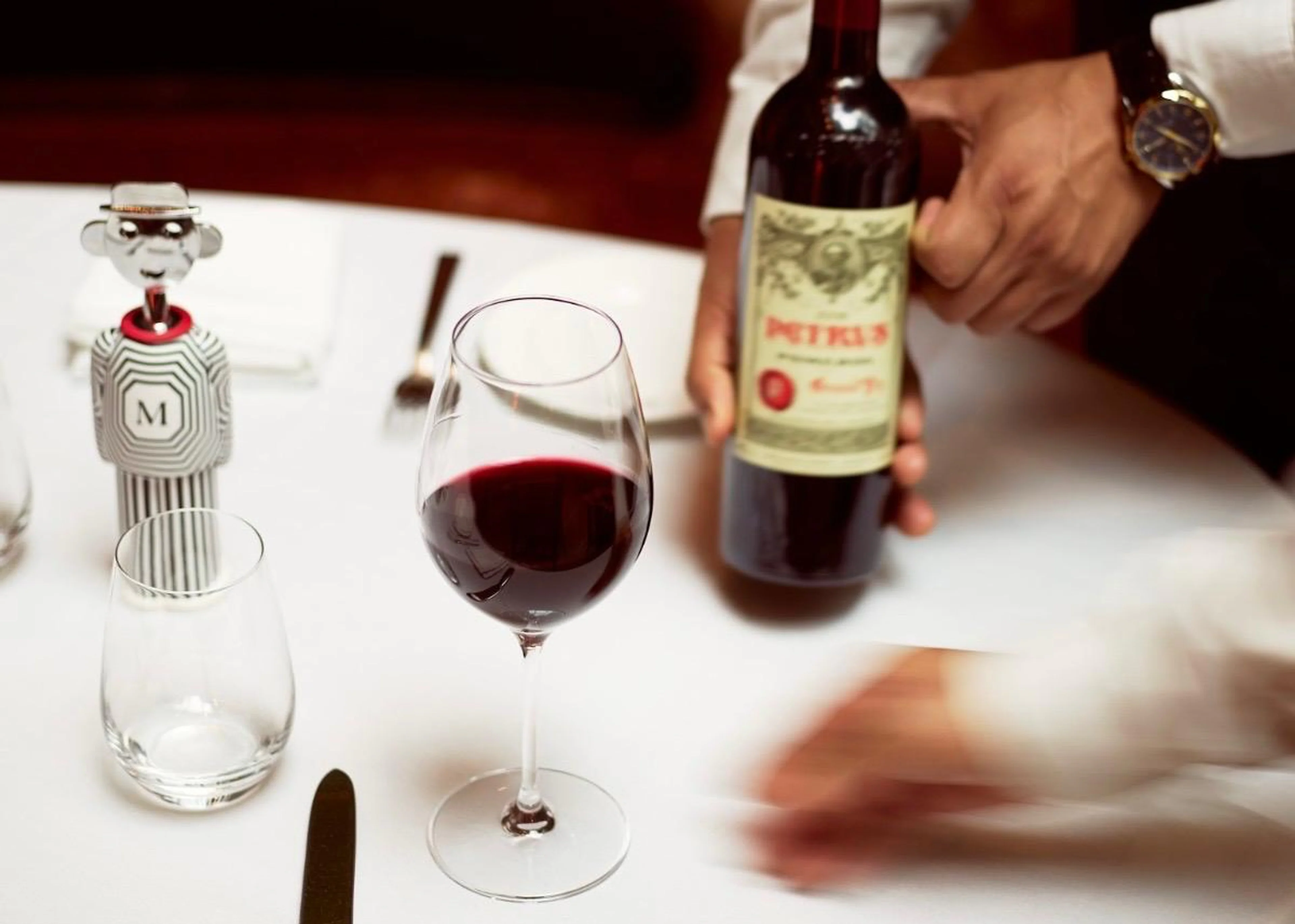 Ein elegant gedeckter Tisch im Hotel The Mark mit einem Glas Rotwein, einer Flasche Petrus Wein und dem schwarz-weiß gestreiften Alessi Alessandro M. Korkenzieher mit einem M auf der Brust.