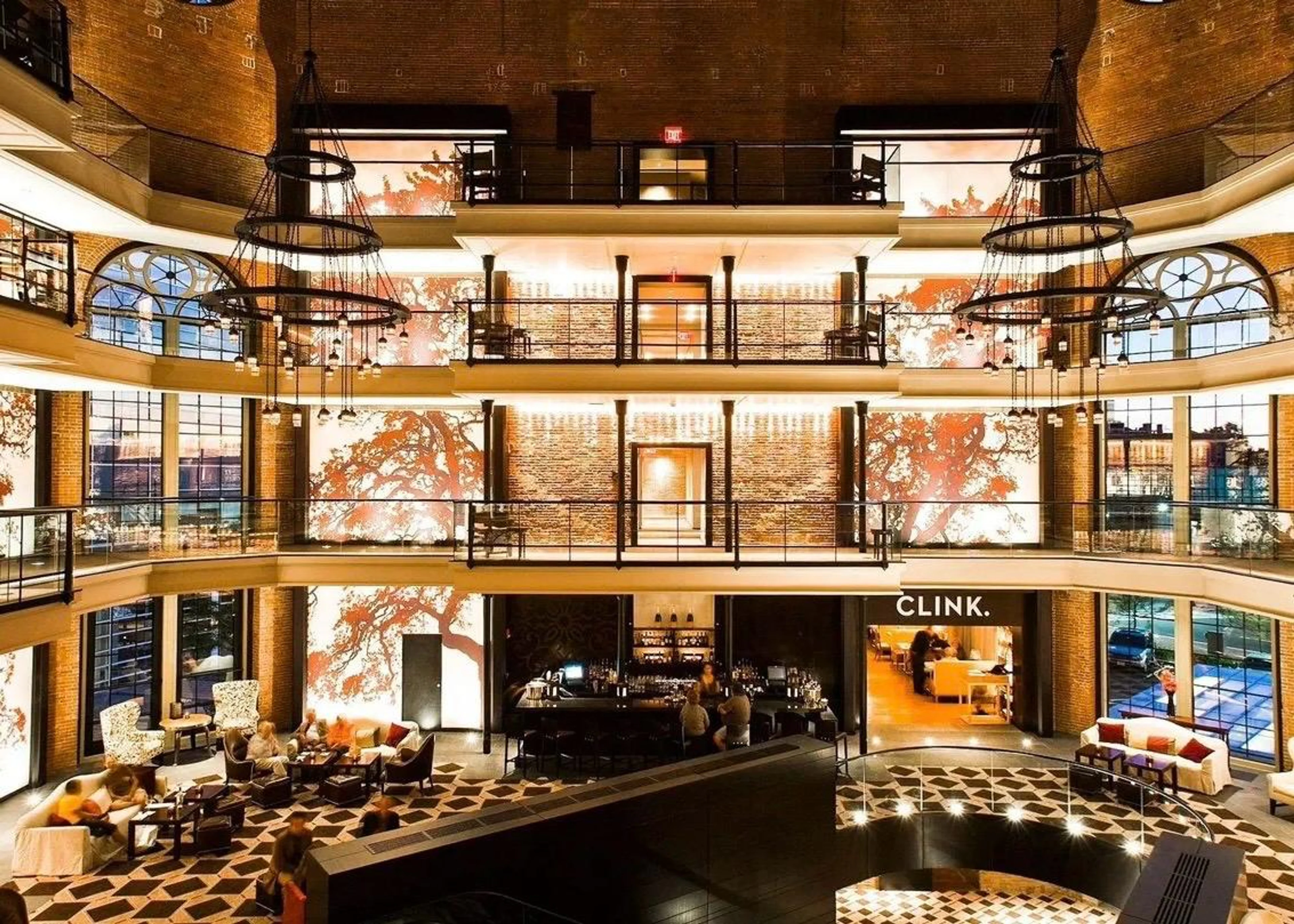 Das mehrstöckige, offene Atrium eines in ein Luxushotel umgewandelten Gefängnisses mit freigelegten Backsteinwänden, runden Kronleuchtern und einer Hotelbar im Erdgeschoss.
