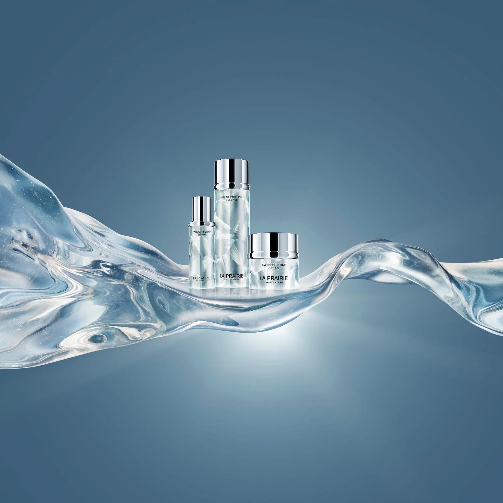 La Prairie Swiss Pristine Pflegelinie: Essence, Serum und Cream Die dreiteilige La Prairie Swiss Pristine Kollektion bestehend aus Essence, Serum und Cream vor einem hellen Hintergrund.