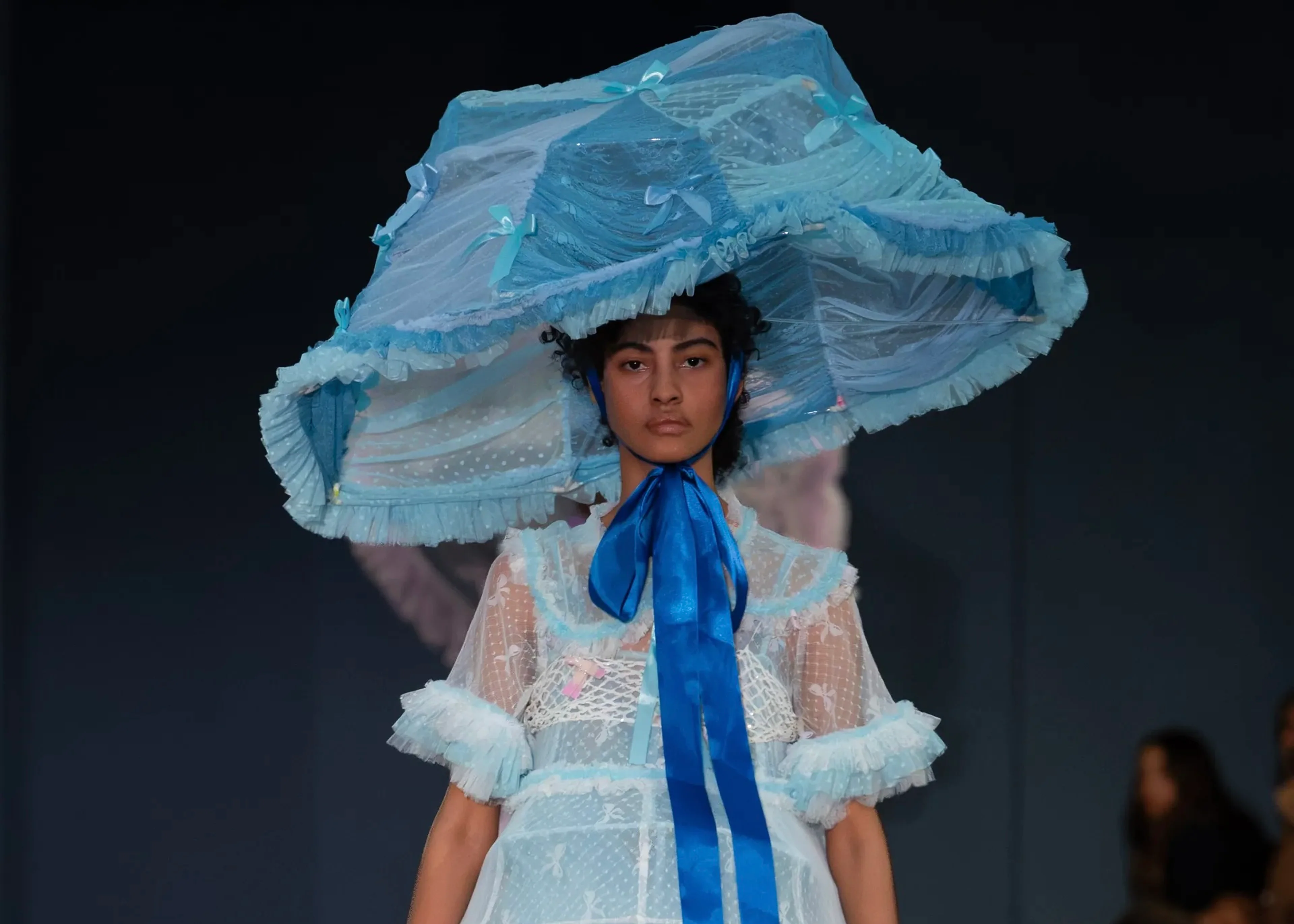 Ein Model präsentiert auf dem Runway in Hyères ein transparentes, hellblaues Kleid mit passendem, übergroßen Hut im Lampenschirm-Stil aus der prämierten ‚Food Cover‘-Kollektion der Designerin Yui Chen.