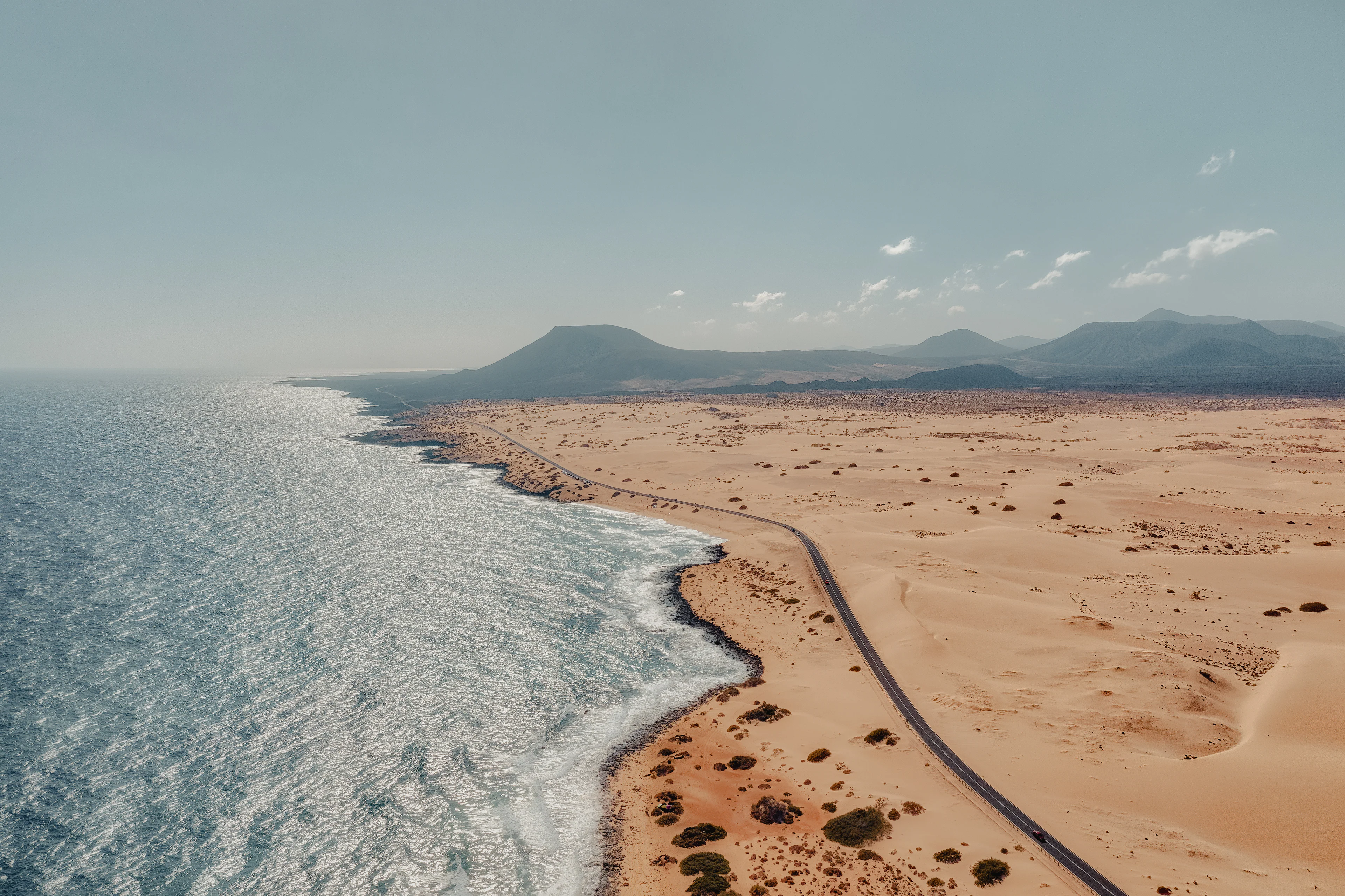 Luftaufnahme der Küstenstraße auf Fuerteventura mit goldenen Sanddünen, felsiger Atlantikküste und vulkanischer Landschaft auf den Kanarischen Inseln.