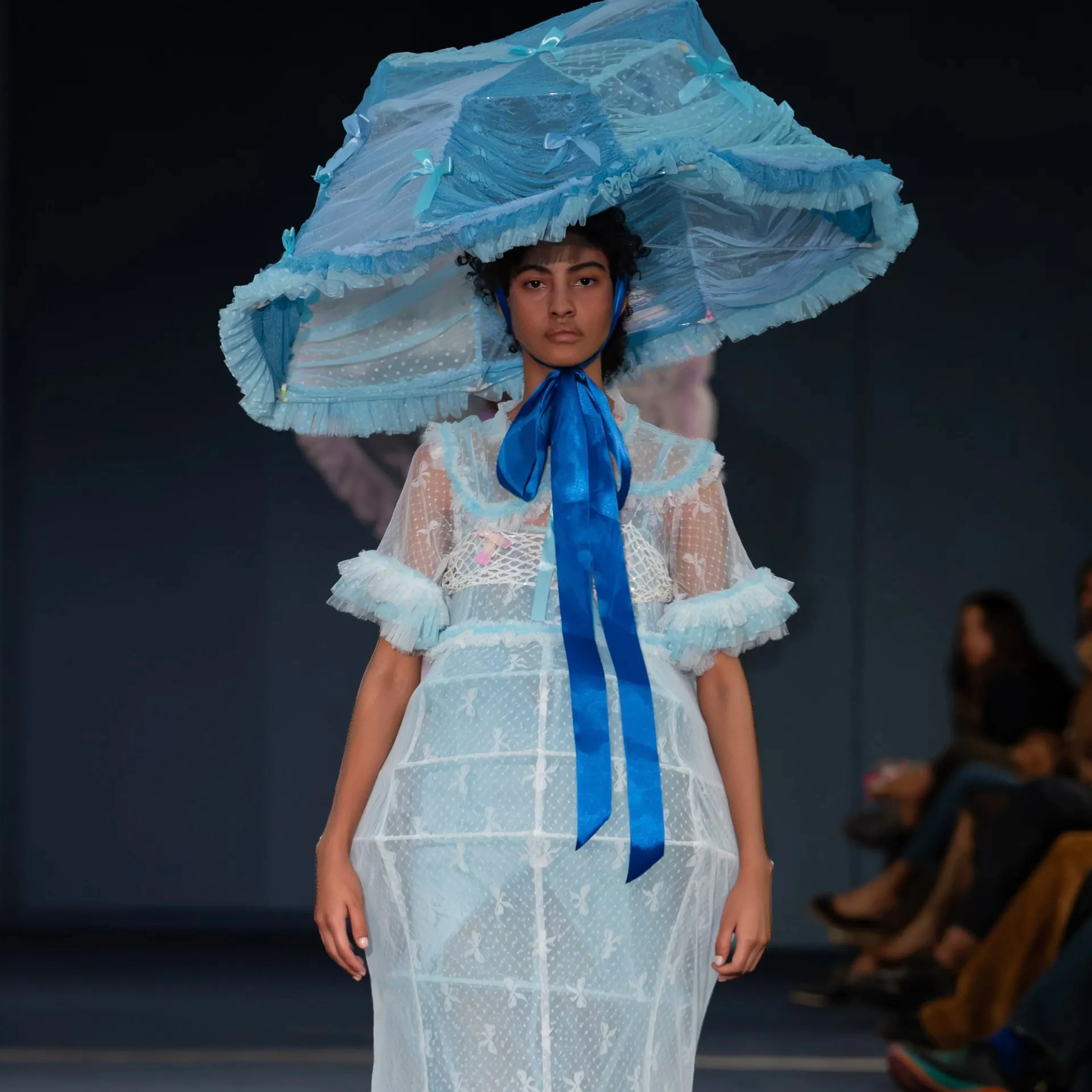 Ein Model präsentiert auf dem Runway in Hyères ein transparentes, hellblaues Kleid mit passendem, übergroßen Hut im Lampenschirm-Stil aus der prämierten ‚Food Cover‘-Kollektion der Designerin Yui Chen.