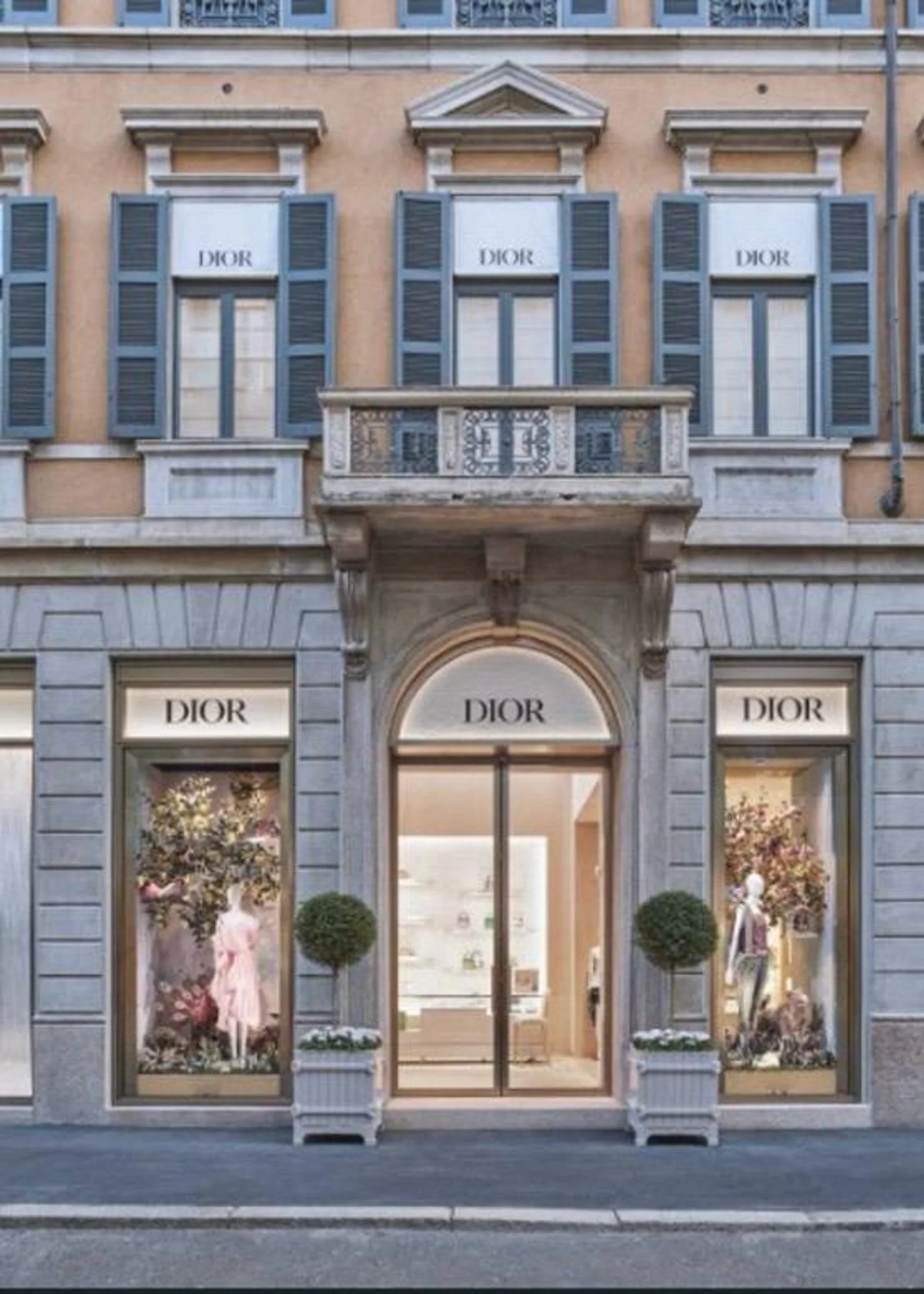 Die elegante Steinfassade des neuen Dior Flagship-Stores in Mailand an der Via Montenapoleone mit großen, beleuchteten Schaufenstern und blauen Fensterläden.
