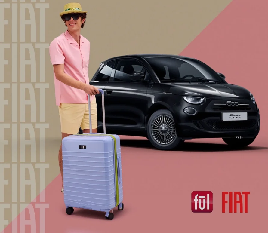 Model mit blauem Reisekoffer aus der Fiat x Ful Kollektion vor schwarzem Fiat 500.