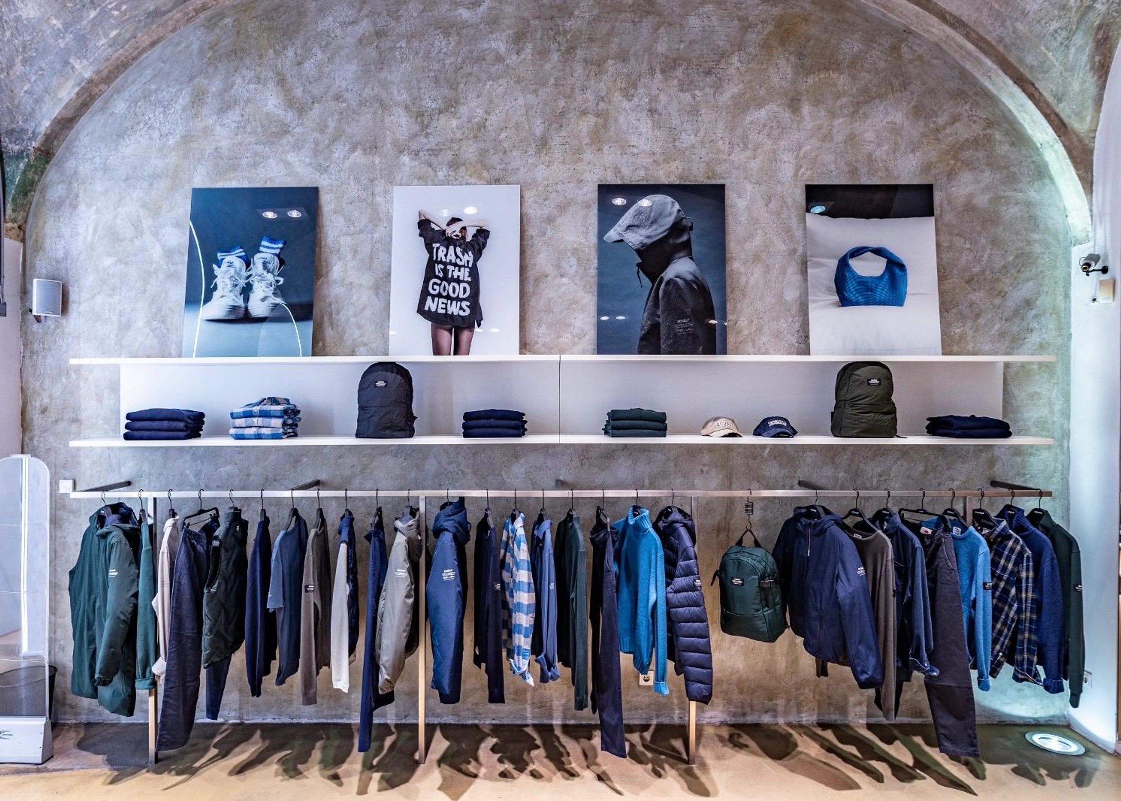 Der Innenraum des Ecoalf Pop-up-Stores in Wien mit ordentlich aufgereihten Jacken, Pullovern und Rucksäcken an einer Kleiderstange vor einer Sichtbetonwand.