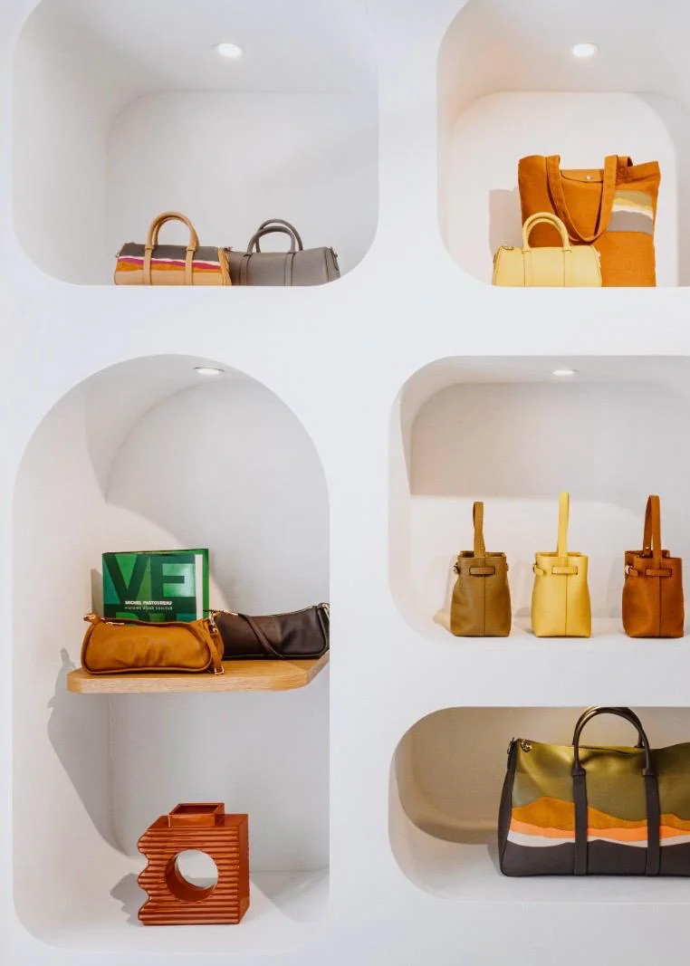 Elegantes weißes Regal mit geschwungenen Nischen im neuen Longchamp Store auf Capri, bestückt mit verschiedenen Designer-Handtaschen in sommerlichen Farben wie Gelb, Braun und Grün.