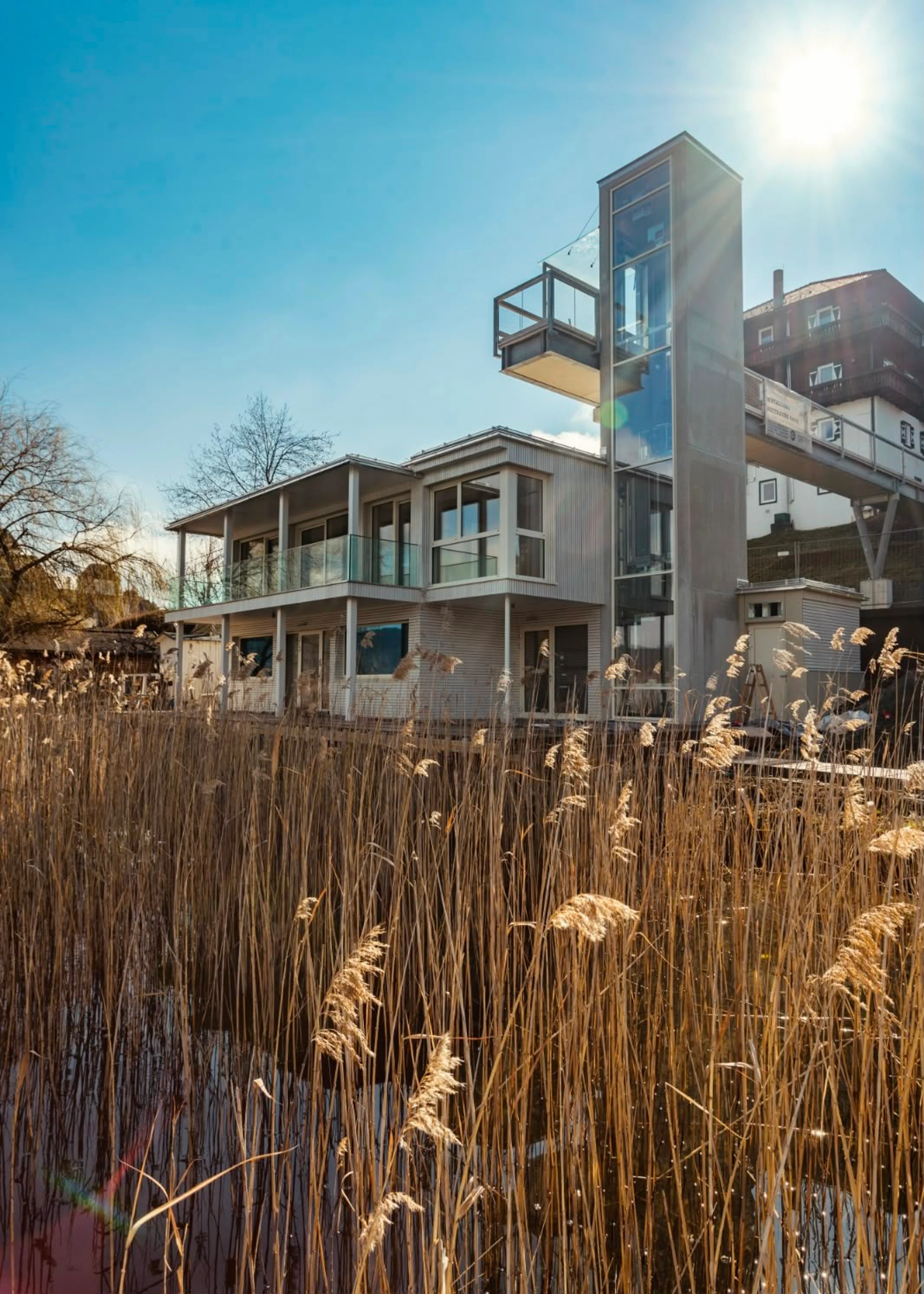 Modernes Badehaus des Original FX Mayr Health Centers am Wörthersee mit großen Fensterflächen und Schilf im Vordergrund.