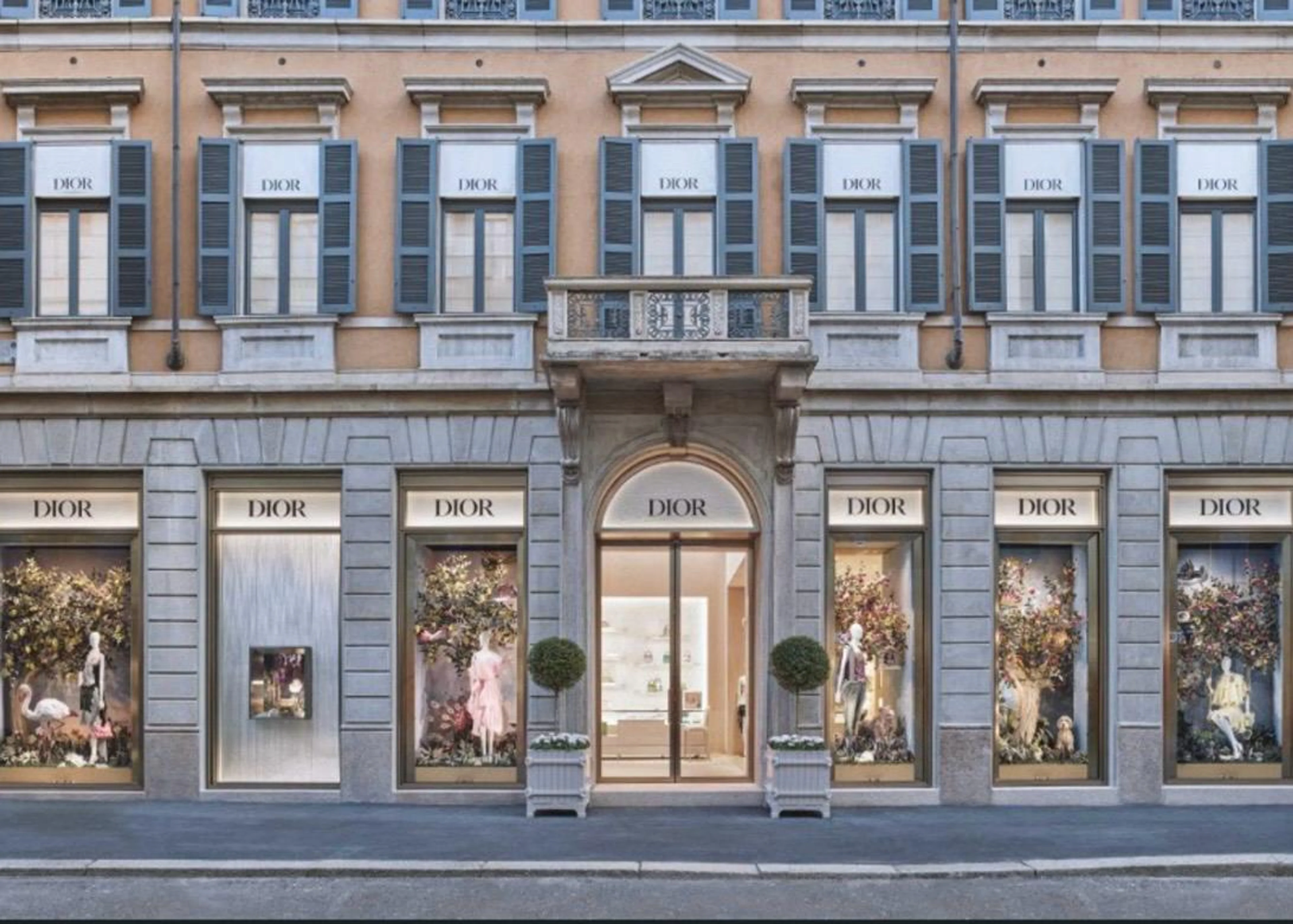 Die elegante Steinfassade des neuen Dior Flagship-Stores in Mailand an der Via Montenapoleone mit großen, beleuchteten Schaufenstern und blauen Fensterläden.