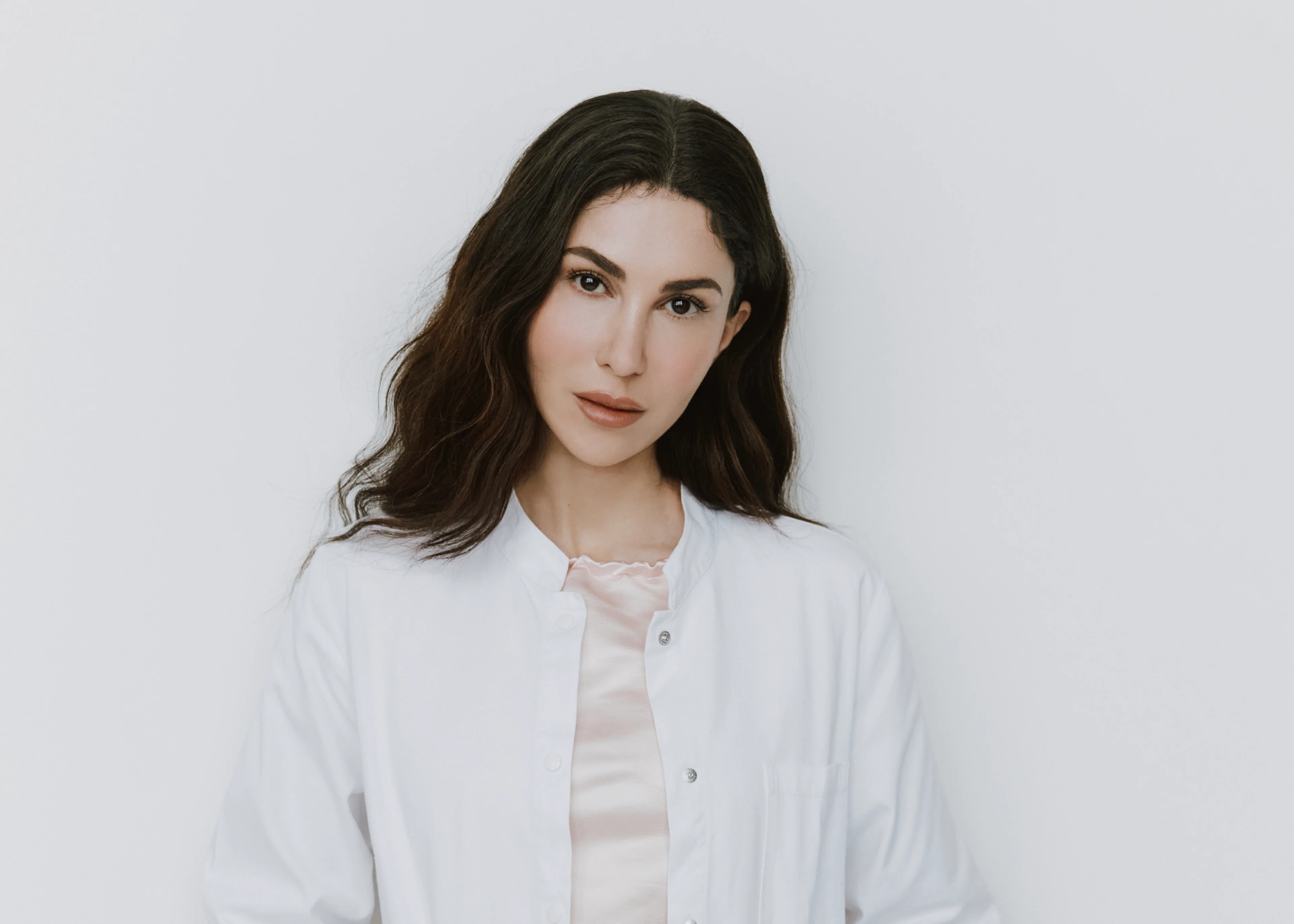 Porträt der Dermatologin Dr. Emi Arpa im weißen Arztkittel vor hellem Hintergrund für ein Interview über Hautgesundheit und Skincare.