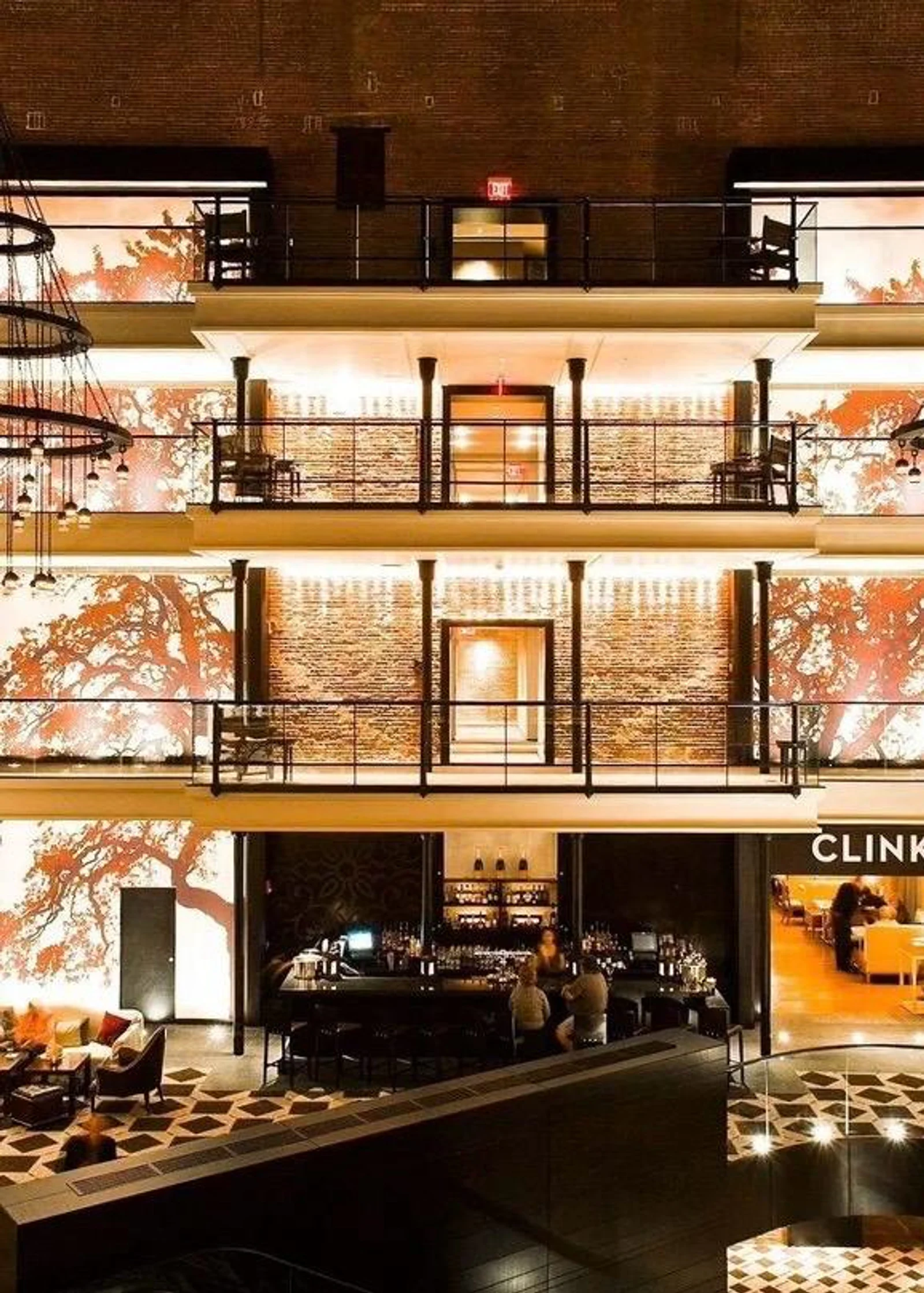Das mehrstöckige, offene Atrium eines in ein Luxushotel umgewandelten Gefängnisses mit freigelegten Backsteinwänden, runden Kronleuchtern und einer Hotelbar im Erdgeschoss.