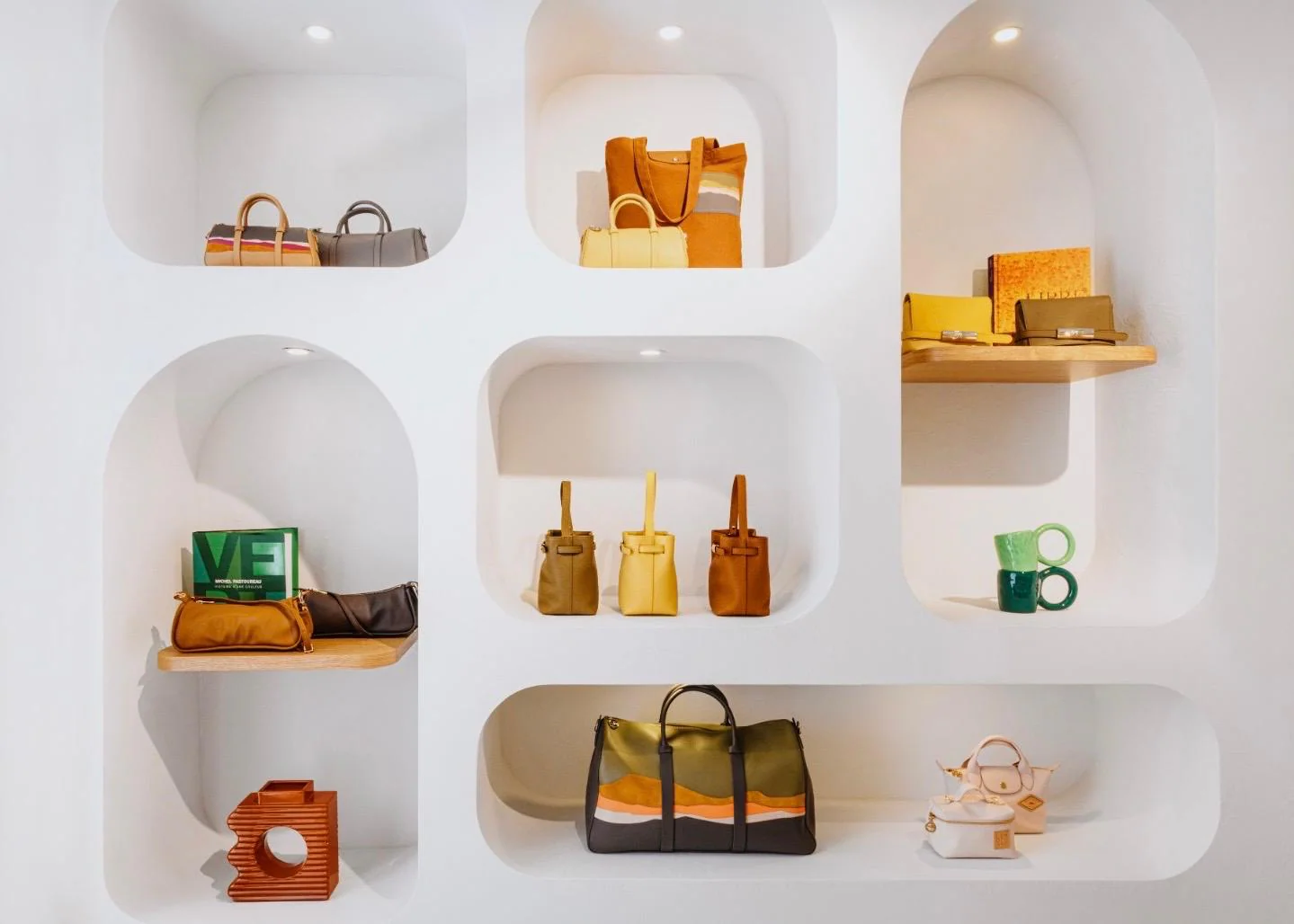 Elegantes weißes Regal mit geschwungenen Nischen im neuen Longchamp Store auf Capri, bestückt mit verschiedenen Designer-Handtaschen in sommerlichen Farben wie Gelb, Braun und Grün.