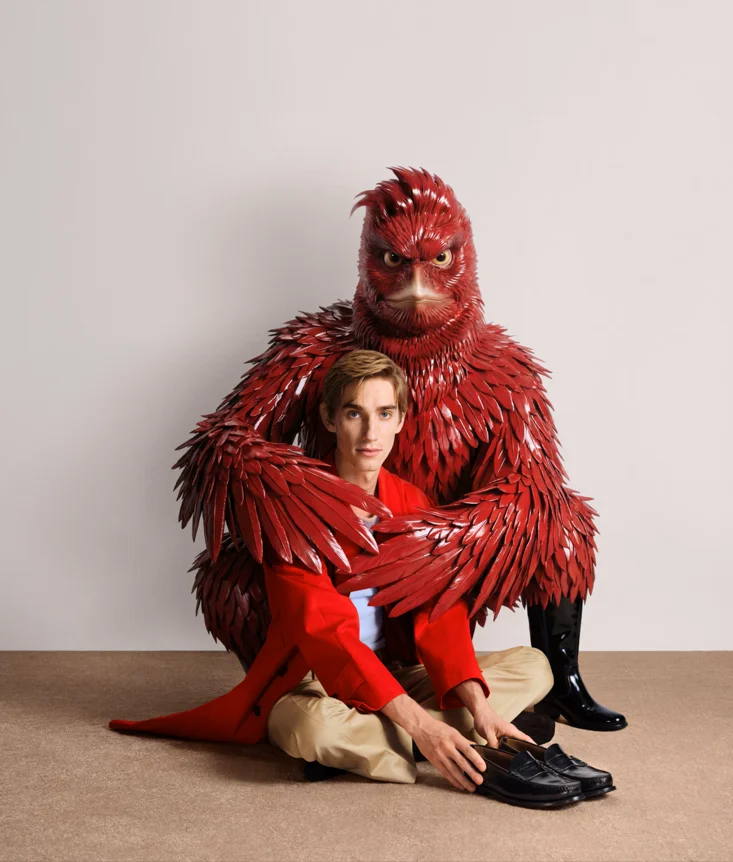 Männliches Model in rotem Mantel vor roter Vogel-Figur aus der Prada Kampagne