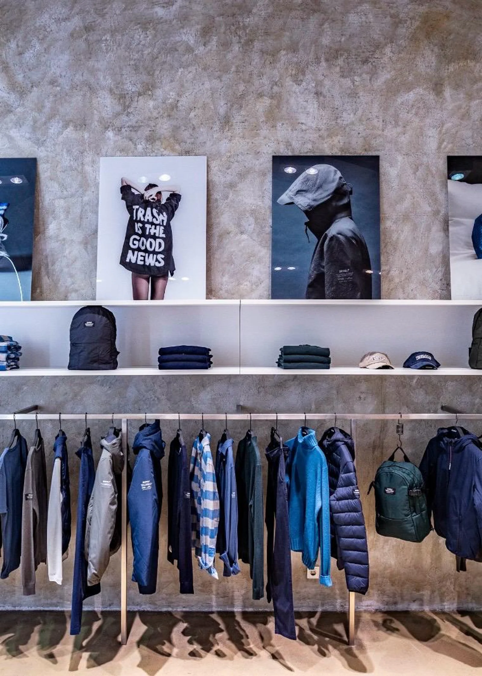 Der Innenraum des Ecoalf Pop-up-Stores in Wien mit ordentlich aufgereihten Jacken, Pullovern und Rucksäcken an einer Kleiderstange vor einer Sichtbetonwand.