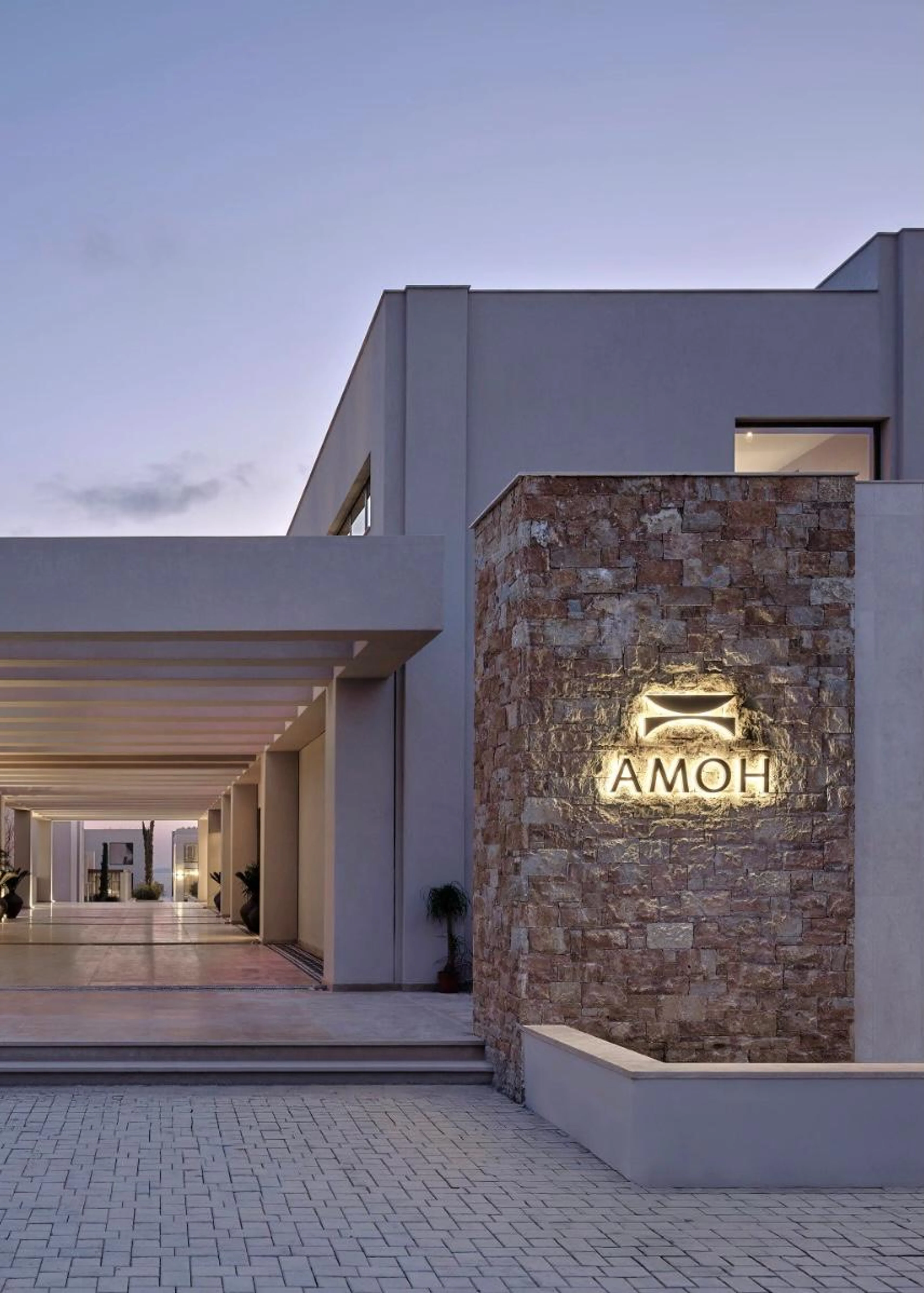 Außenansicht des AMOH Luxury Collection Resort auf Rhodos in der Dämmerung mit moderner Architektur, Natursteinfassaden und stimmungsvoller Beleuchtung.