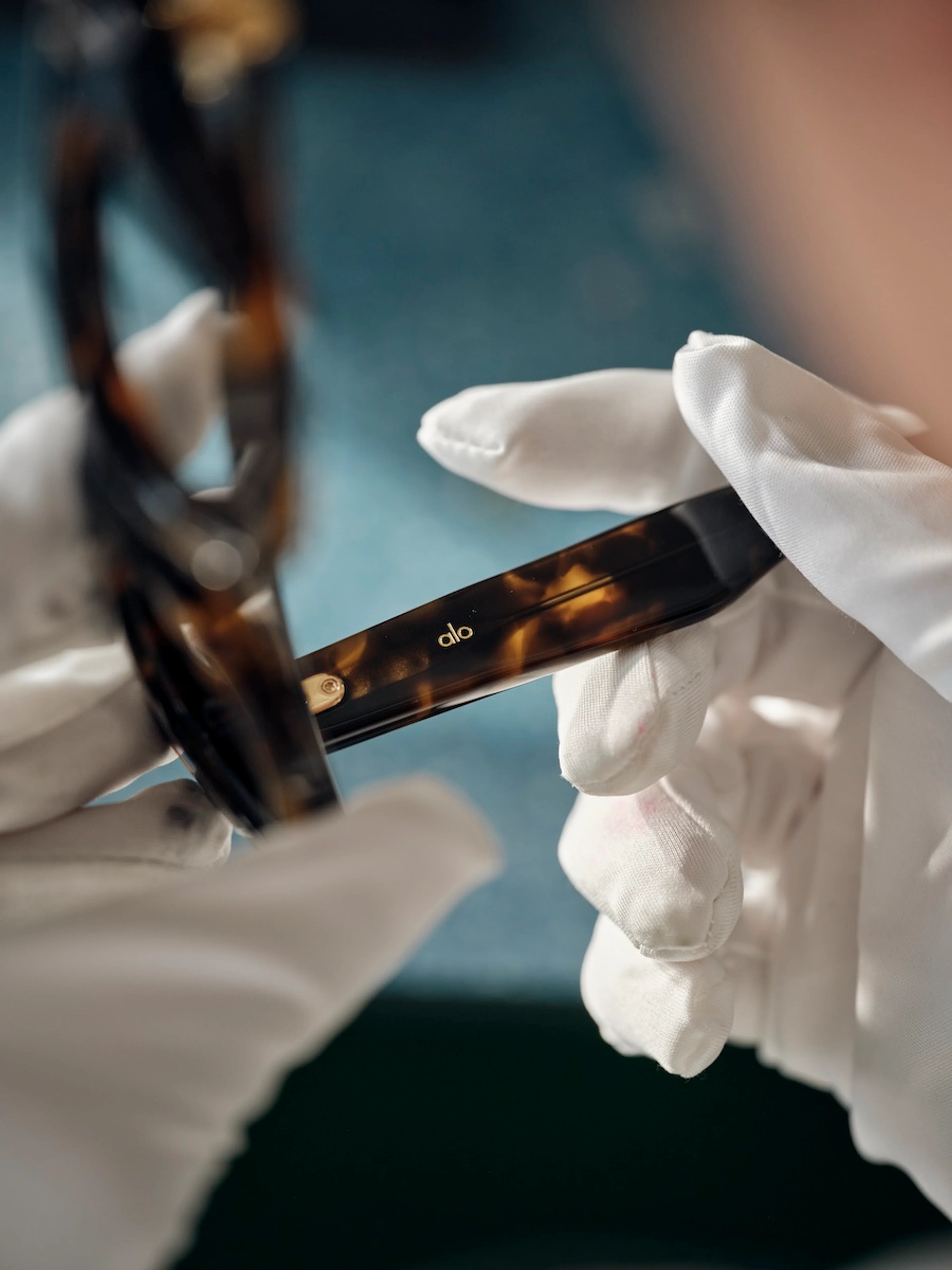 Nahaufnahme einer Sonnenbrille aus der Alo Eyewear-Kollektion, die in den Händen gehalten wird.