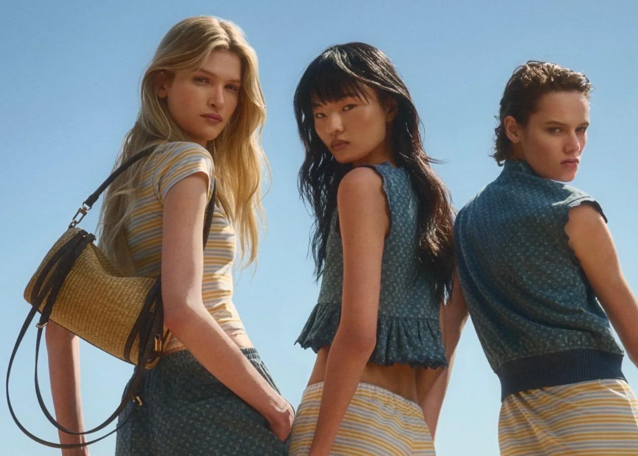 Drei Models in sommerlicher Louis Vuitton Kleidung vor blauem Himmel. Links ein gestreiftes T-Shirt mit einer Raffia-Schultertasche, mittig und rechts blaue Denim-Schößchen-Tops mit Flower-Minigram-Muster.