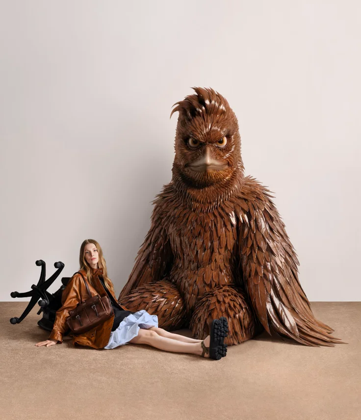 Weibliches Model mit brauner Prada Tasche neben großer brauner Vogel-Figur aus der Jordan Wolfson Kampagne