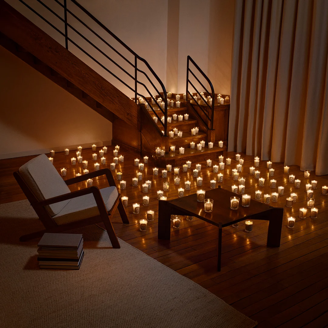 Wohnraum mit vielen brennenden Diptyque Kerzen auf Holzboden und Treppe, neue nachfüllbare Luxus Duftkerze im Design Interior