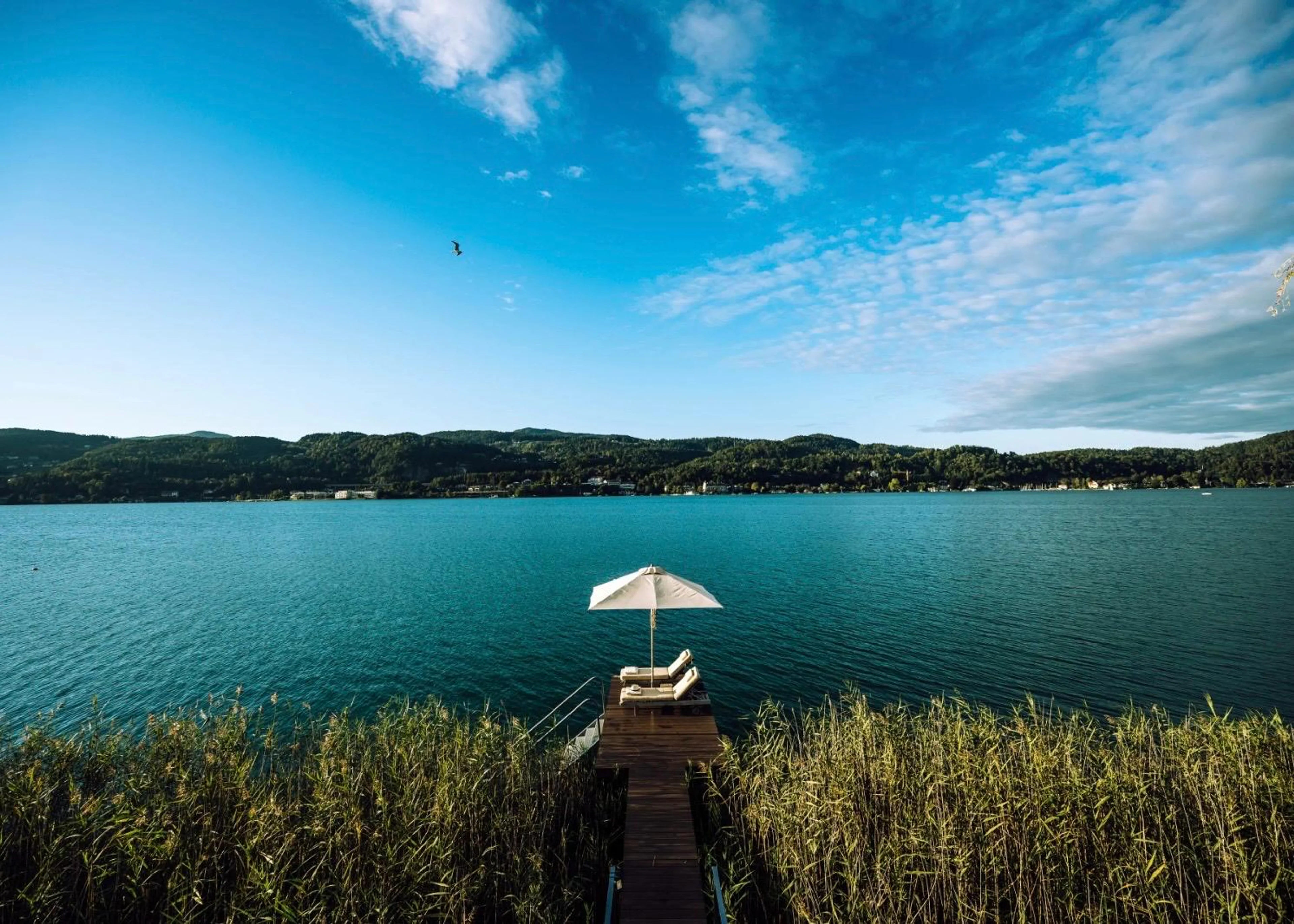 Steg mit Sonnenliegen am See vor der Kulisse des Original FX Mayr Health Centers am Wörthersee.