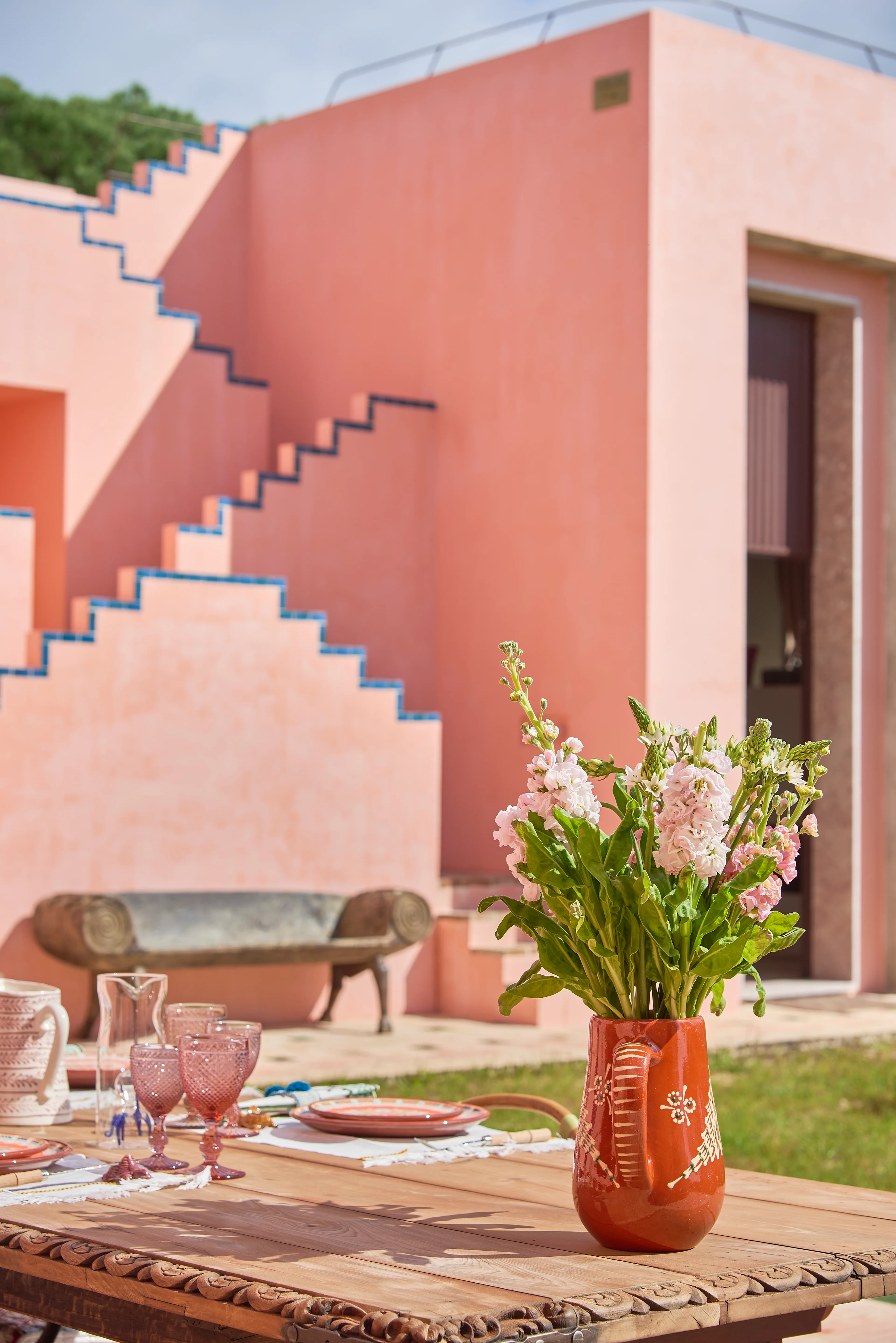Terrasse des Boutiquehotels Vermelho Melides mit rosafarbener Architektur, gedecktem Tisch und portugiesischem Design.