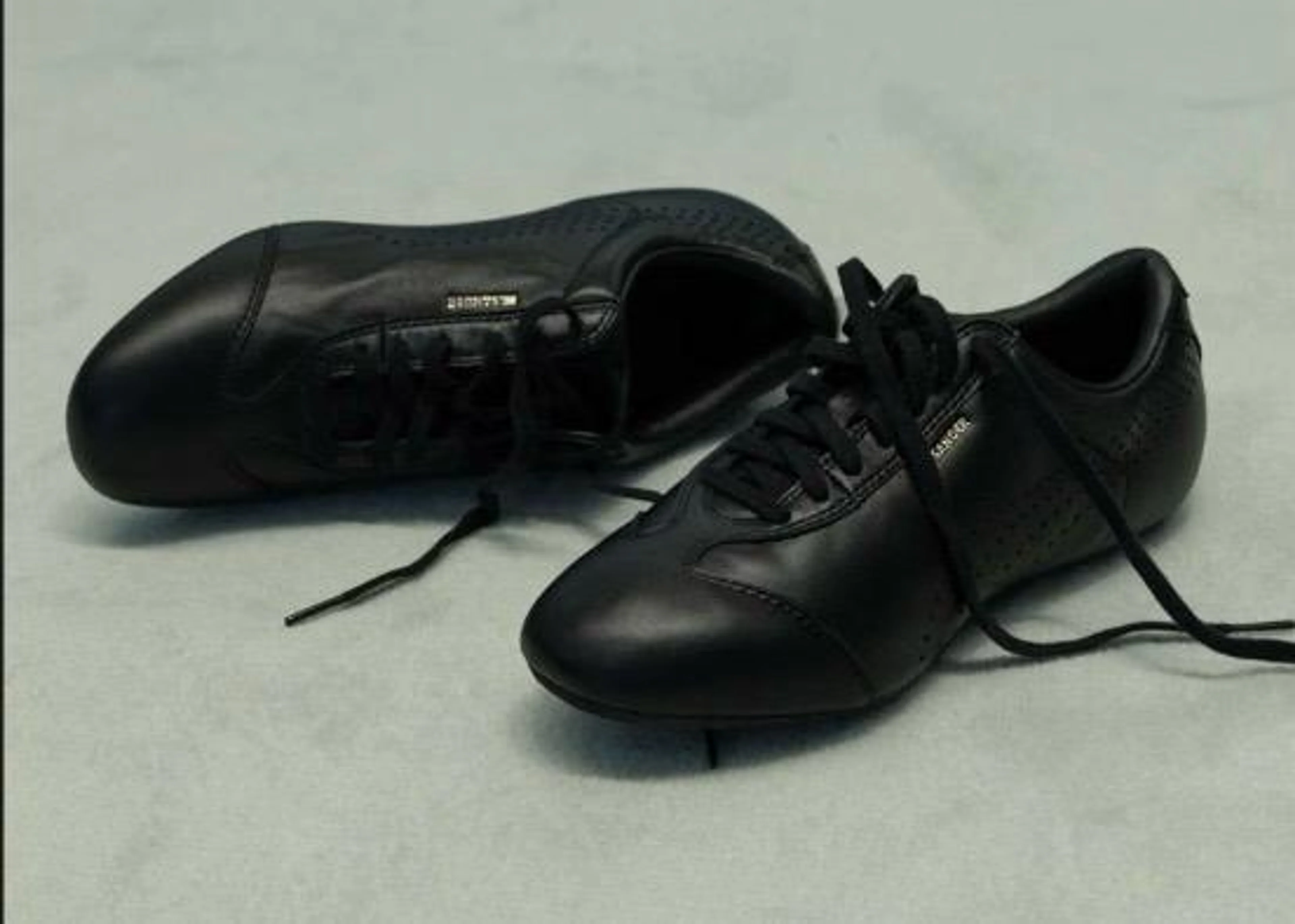Ein Paar schwarze Jil Sander x Puma Speedcat Sneaker aus Glattleder mit feiner Perforation und einem kleinen goldenen Jil Sander Logo an der Schnürung.